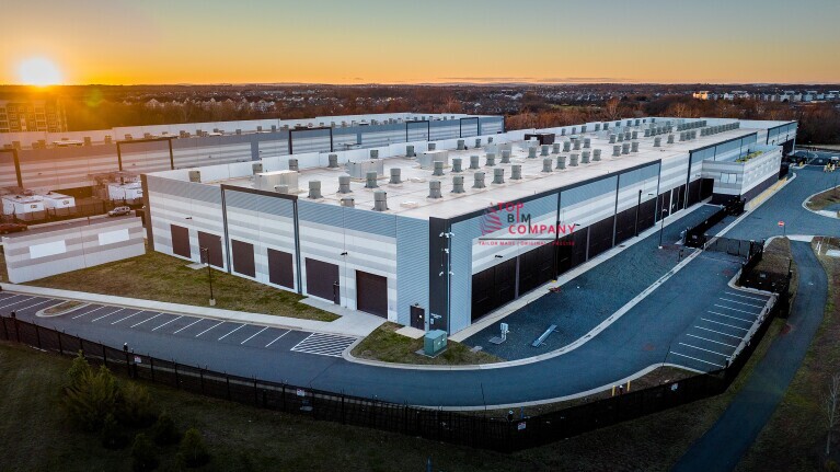 BIM Utility Modeling and Coordination services Exterior view of a completed data center facility with rooftop equipment, parking space, and secured fencing, captured during sunset